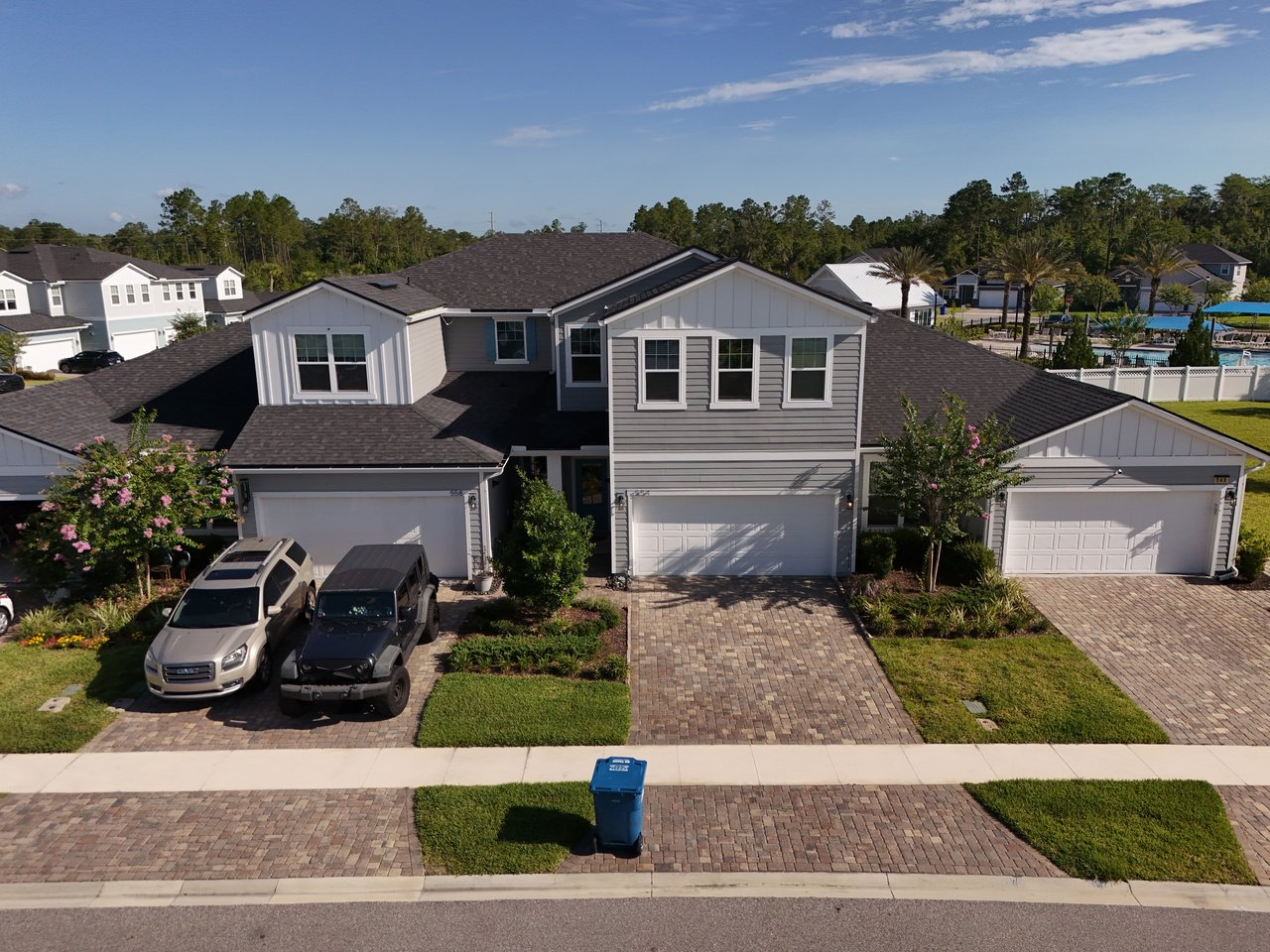 Gray-and-white two-story home with a paver driveway and neighboring houses behind it.