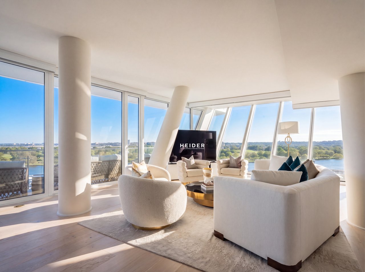 Living room with white sofas, floor-to-ceiling windows, and views of water and parkland.