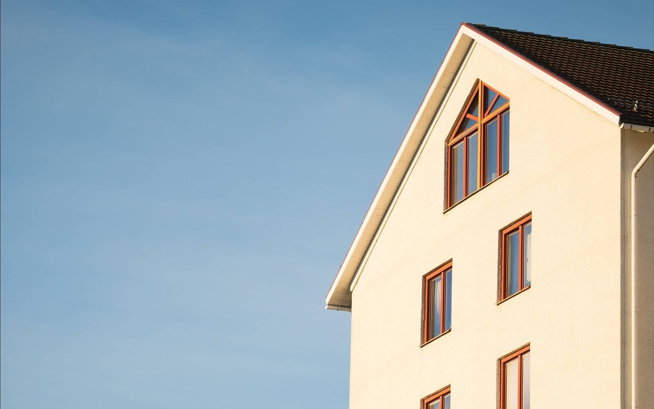 White multi-story house with a steep gable, dark tiled roof, and reddish-brown window frames.