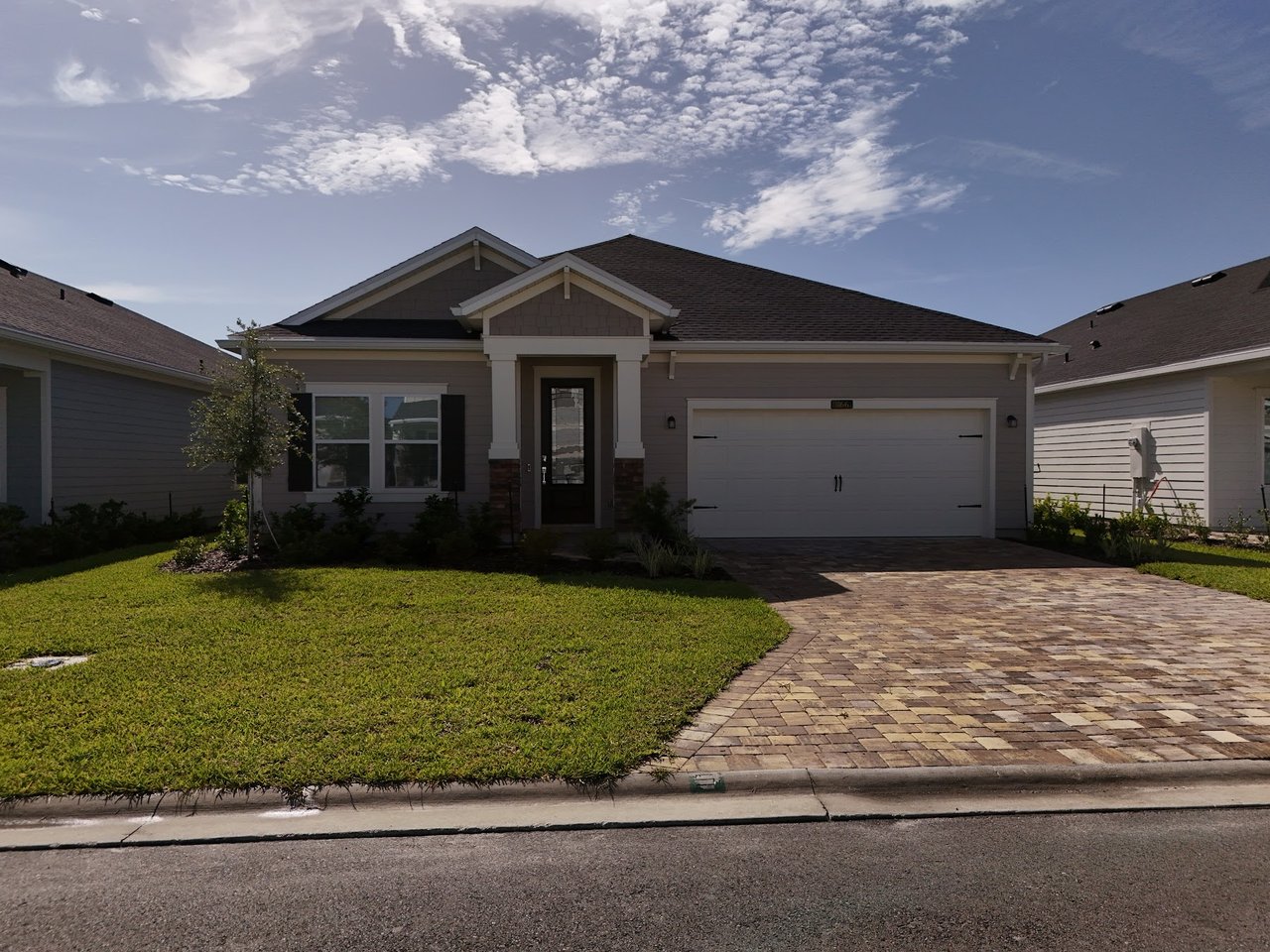 Gray single-story home with a two-car garage, green lawn, and broad paver driveway.