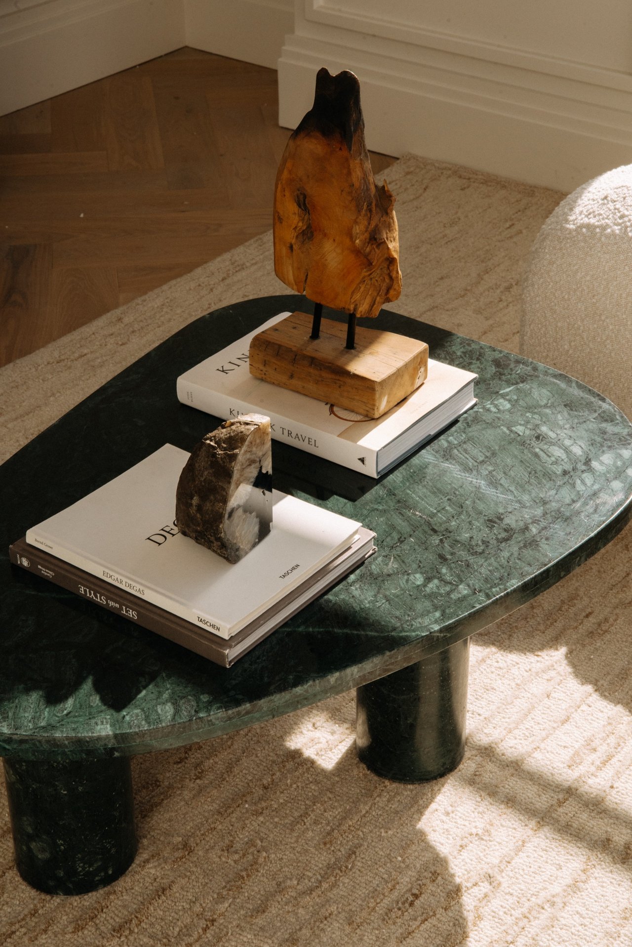 Green marble coffee table with art books and sculptural decor on a cream rug.