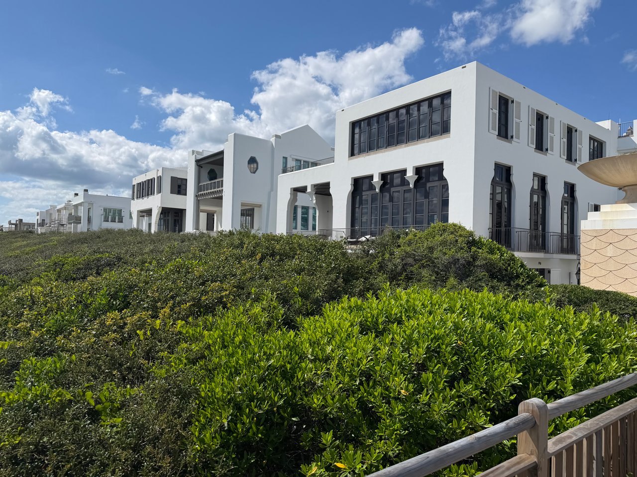 Stunning three-story white luxury homes with black window frames overlooking lush green coastal vegetation in Alys Beach.