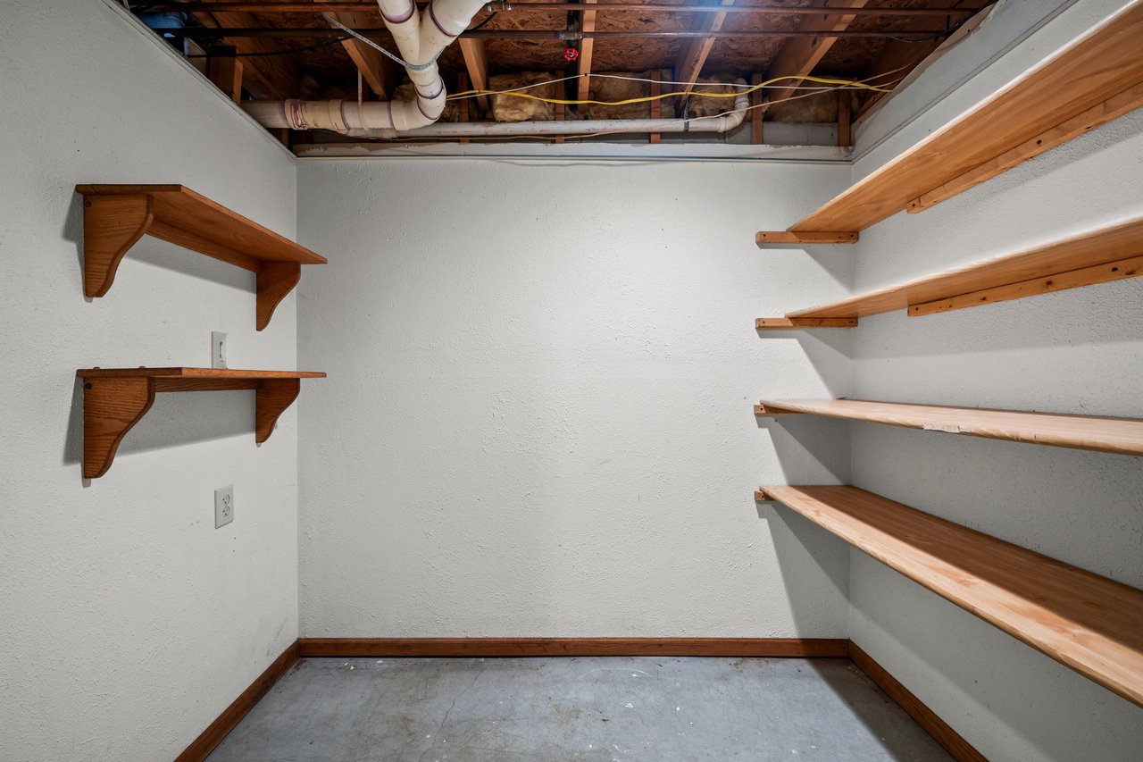 Empty storage closet with wooden shelving and an exposed ceiling.