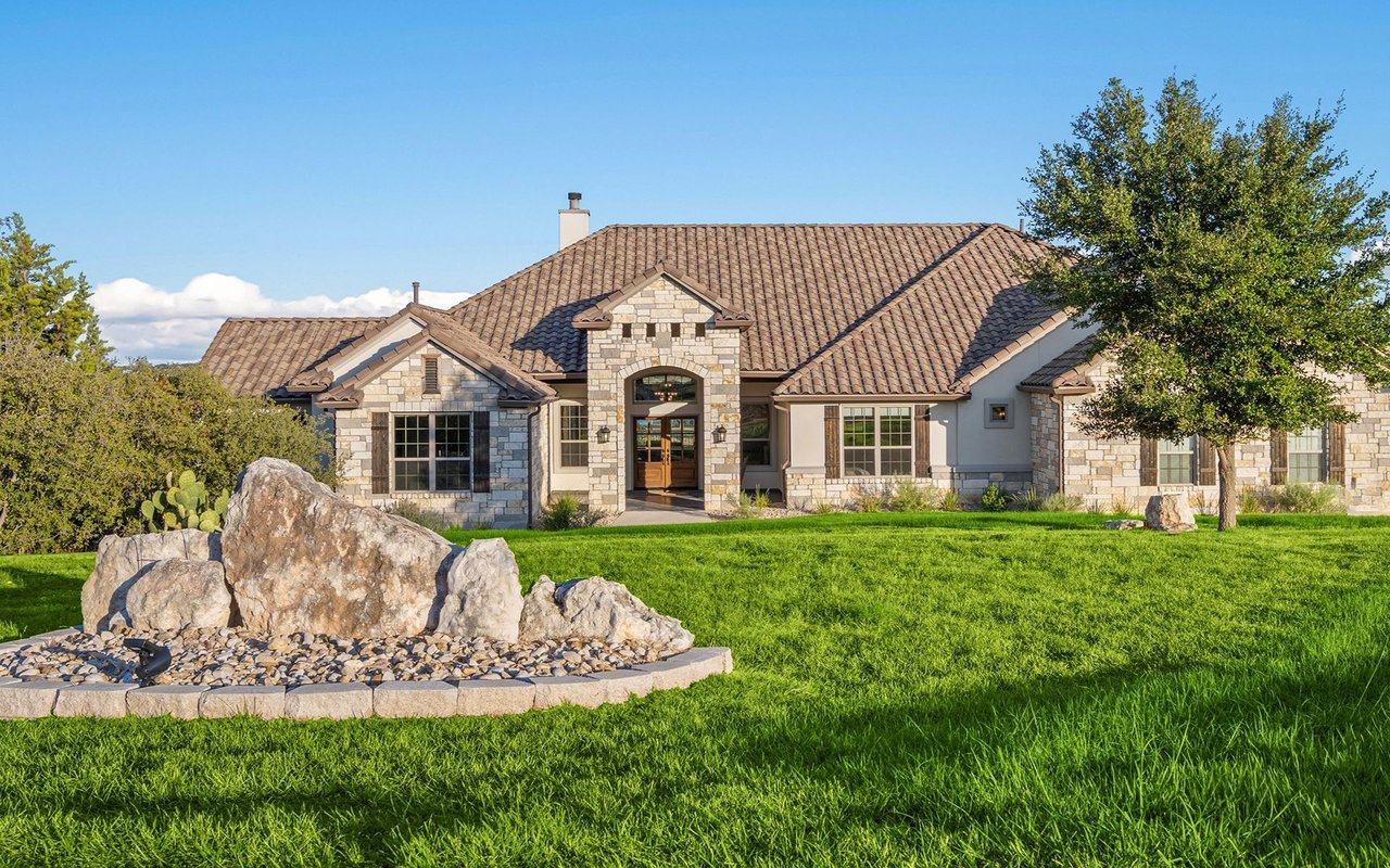 Stone-and-stucco home with a tiled roof, mature oak tree, and landscaped rock garden.