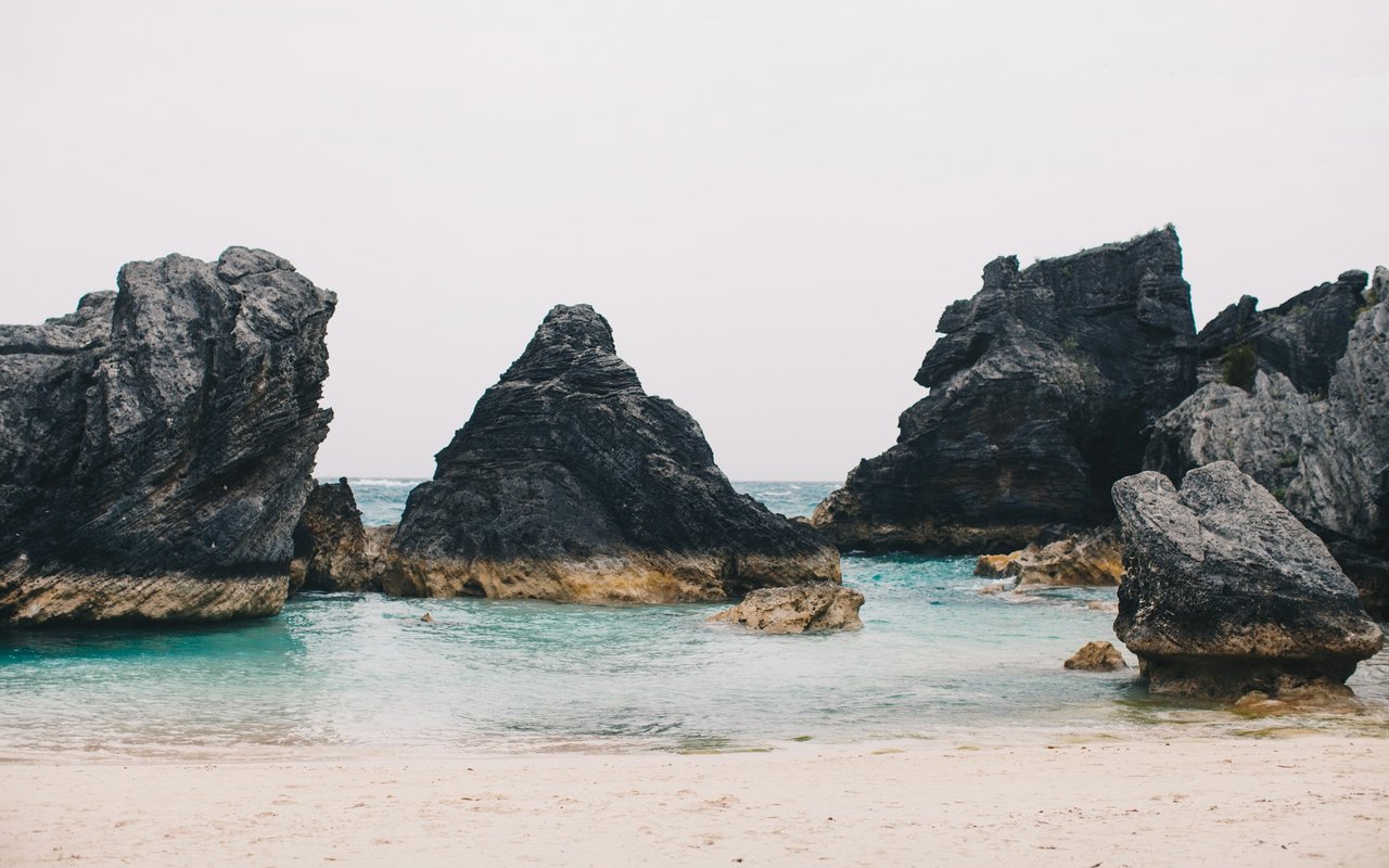 Sandy cove with turquoise water enclosed by dark rock formations.