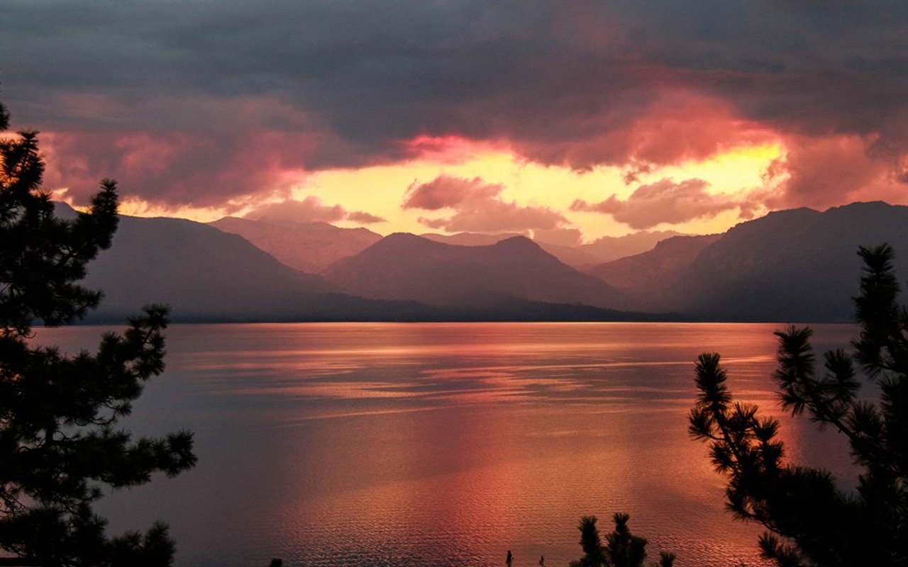 Lake Tahoe at sunset, with orange reflections on the water and mountains silhouetted against a glowing sky.