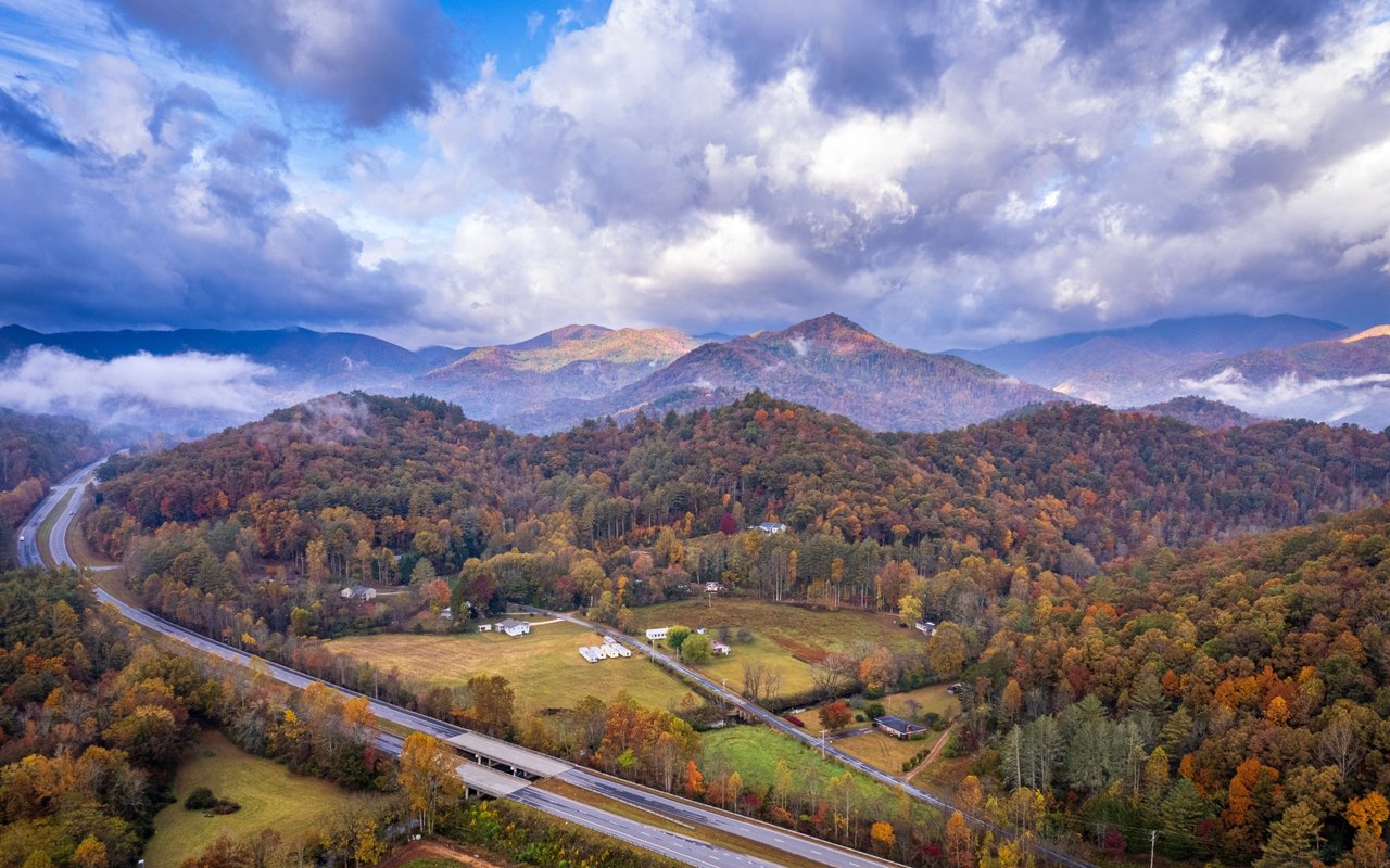 Autumn mountain ridges and wooded hills above a winding highway and scattered rural buildings.