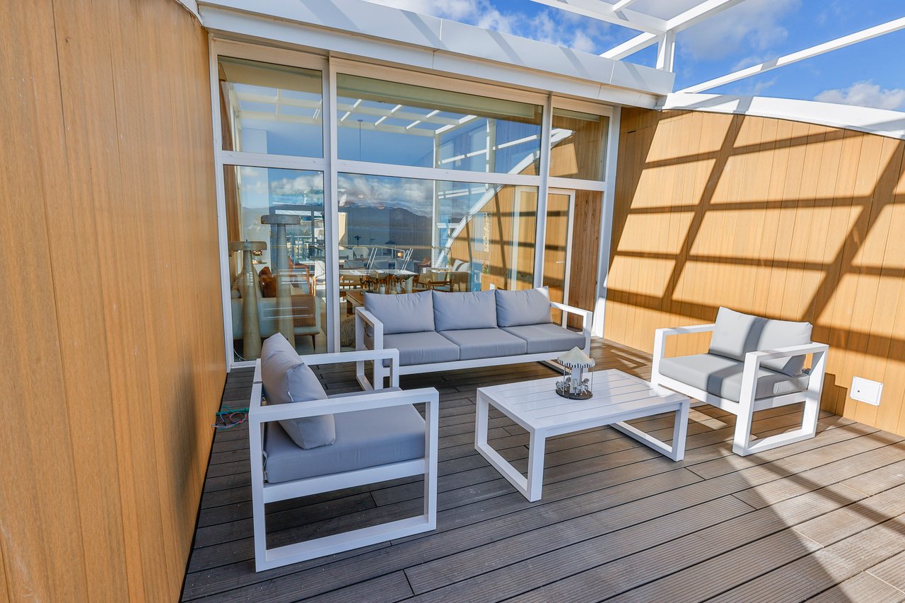 Apartment terrace with white lounge furniture on a wood deck beside expansive glass doors.