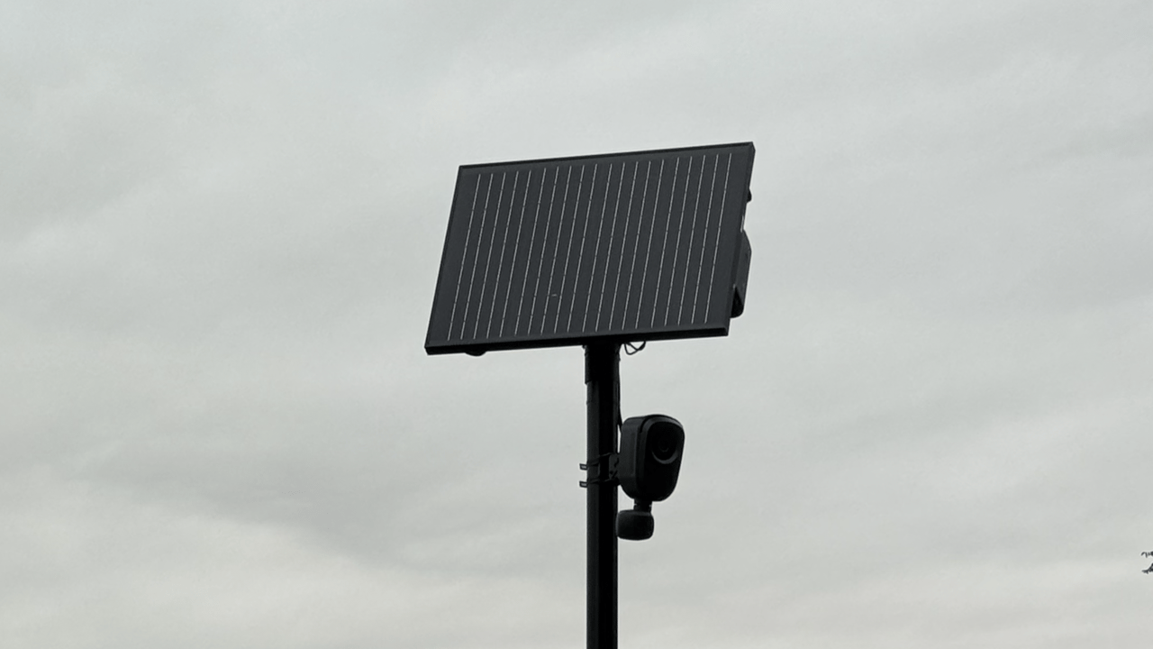 Close-up view of a solar-powered Flock Safety ALPR camera and solar panel array mounted on a standalone black pole.