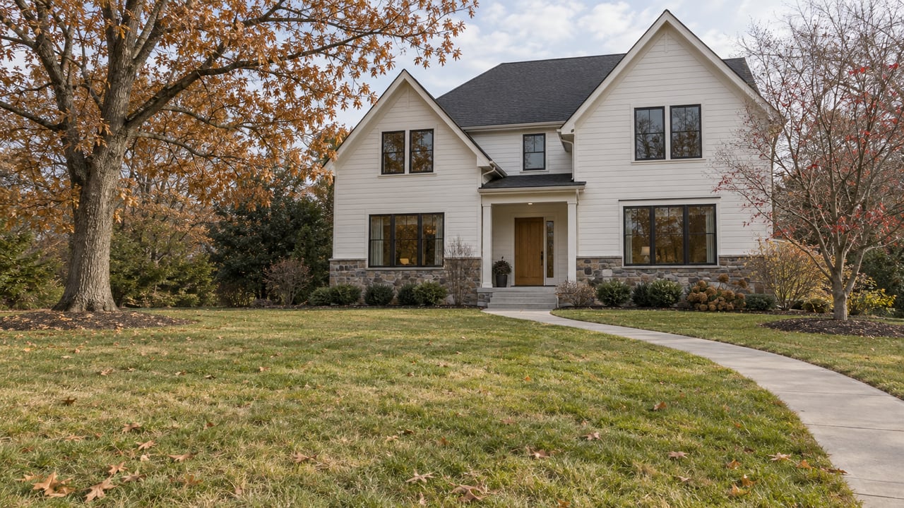 Light-sided gabled home with a stone foundation, broad front lawn, and mature late-autumn oak and dogwood trees.