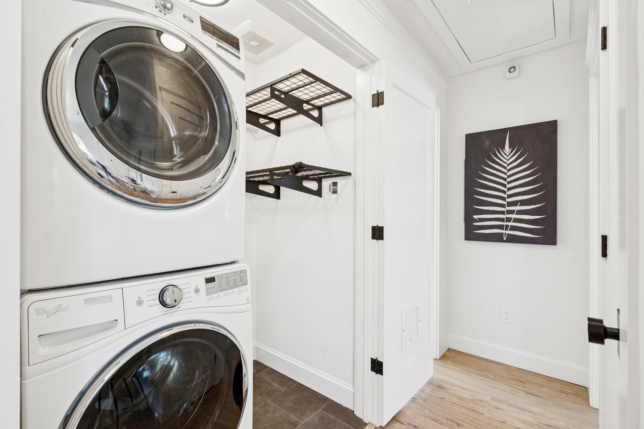 Laundry room with a stacked washer and dryer, black wire shelving, and fern wall art.