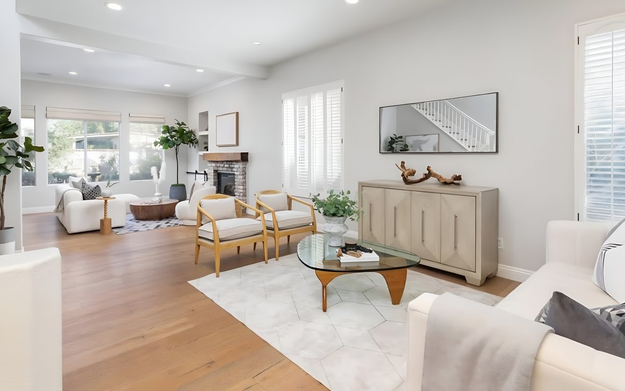 A spacious and modern living room with light wood floors, two white sofas, a gray cabinet, and a framed mirror above it.