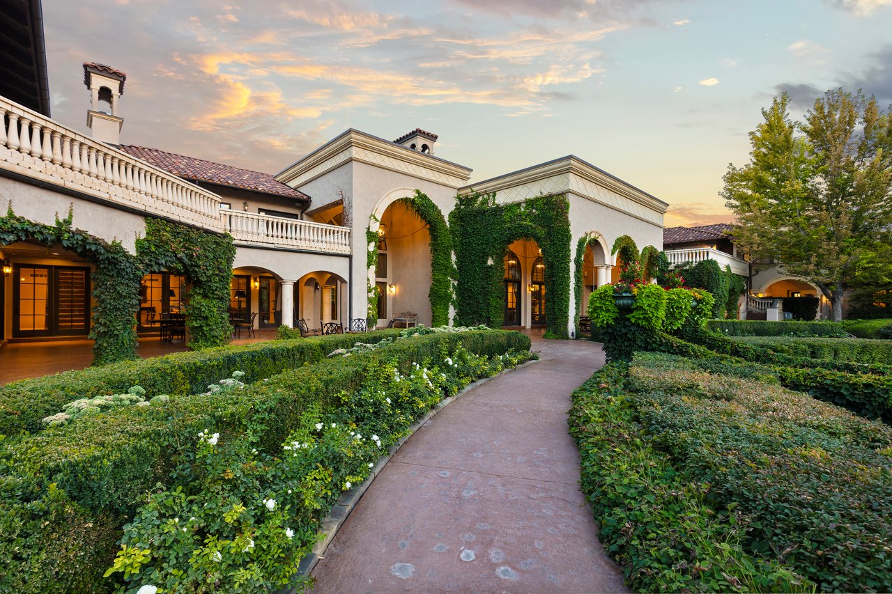 Mediterranean-style home with ivy-covered arches and formal gardens at sunset.