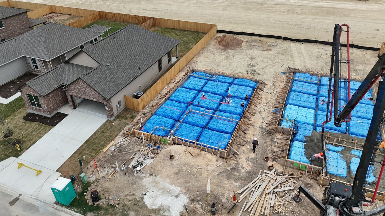 Aerial construction site with two blue-covered house foundations beside completed homes.