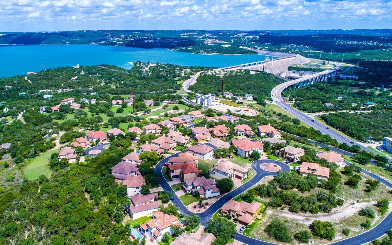 Aerial view of homes beside a lake, with a curved bridge and dam in the distance.