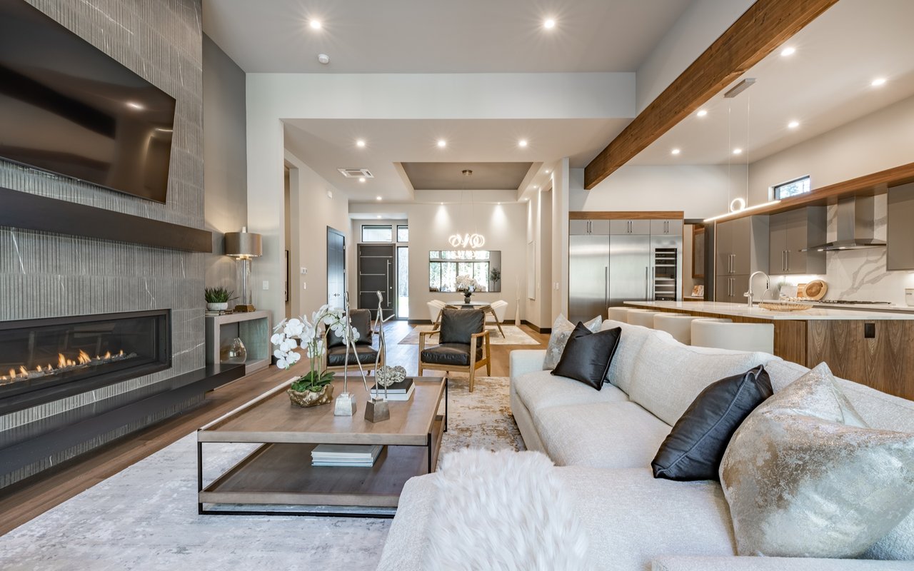 Open-plan living room with a tall tiled fireplace, white sectional, and exposed wood ceiling beams.