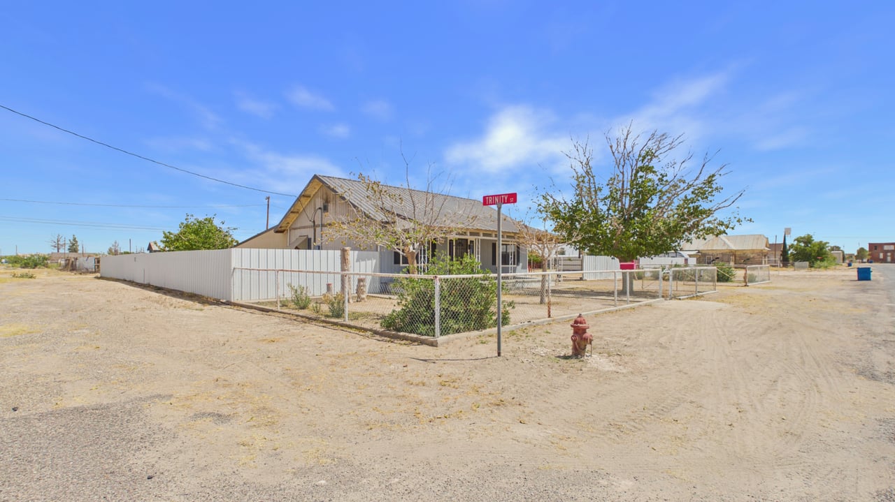 Single-story corner-lot home with white fencing and a chain-link front yard.