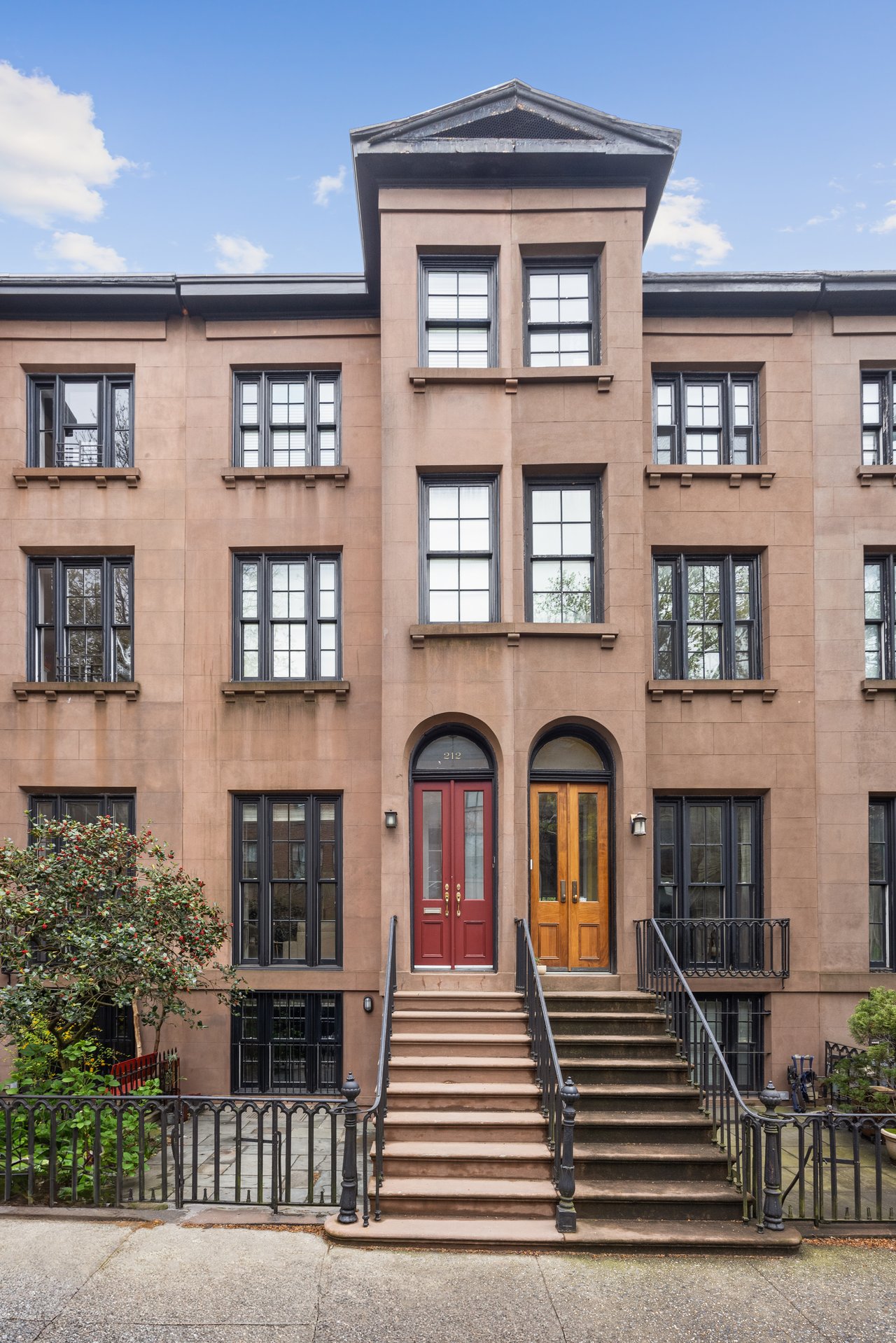 Brownstone townhouse facade with twin stoops and red and wooden entry doors.