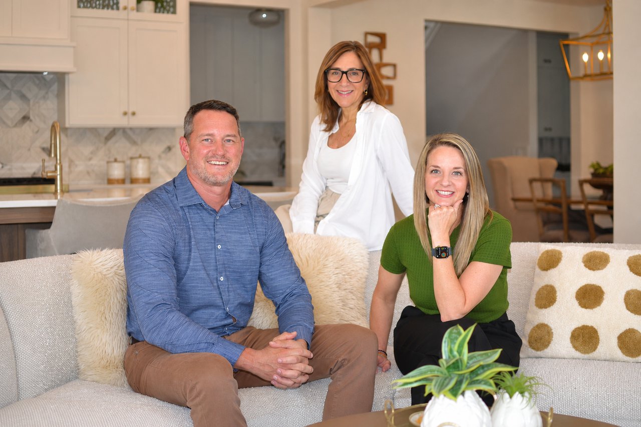 Three real estate professionals pose together in a bright living room and kitchen.
