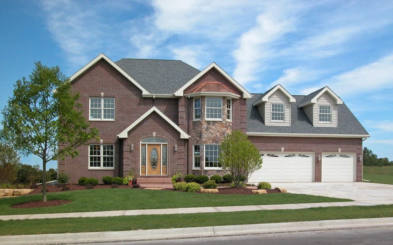 Two-story brick house with stone accents, roof dormers, and an attached three-car garage.