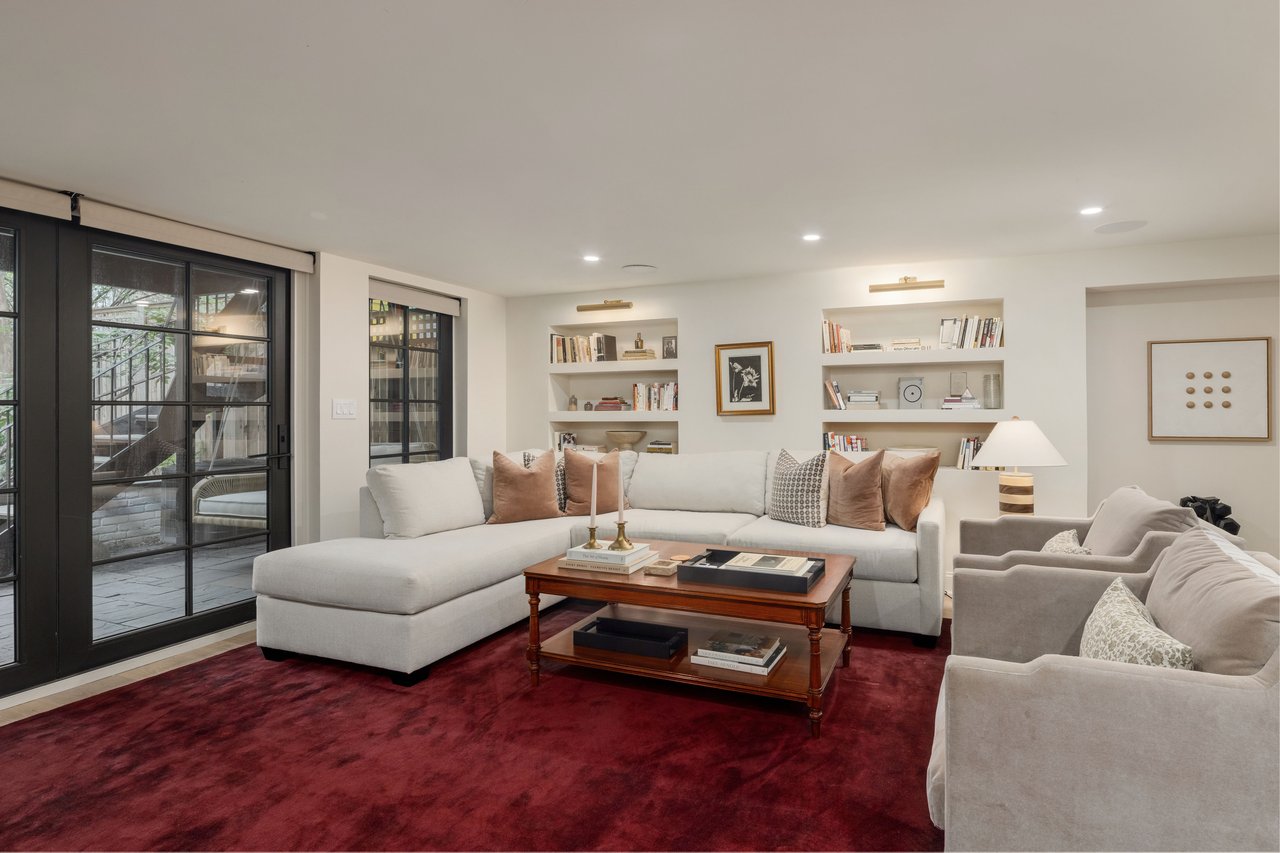 Cozy living room with a white sectional sofa, red rug, built-in shelves, and doors to a patio.
