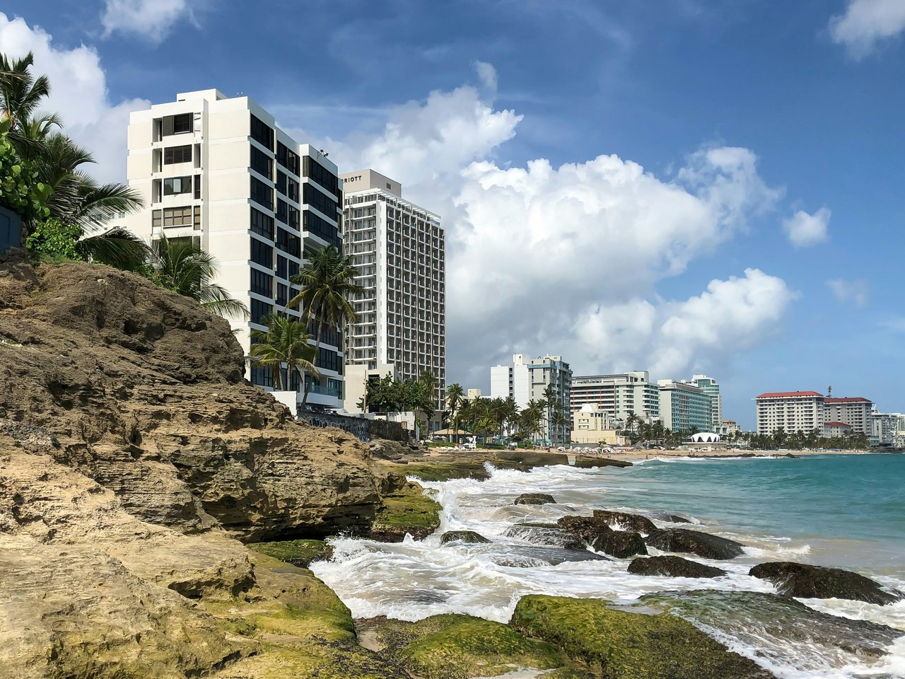 The Condado coastline with modern beachfront hotels, rocky shorelines, and waves crashing against the rocks.