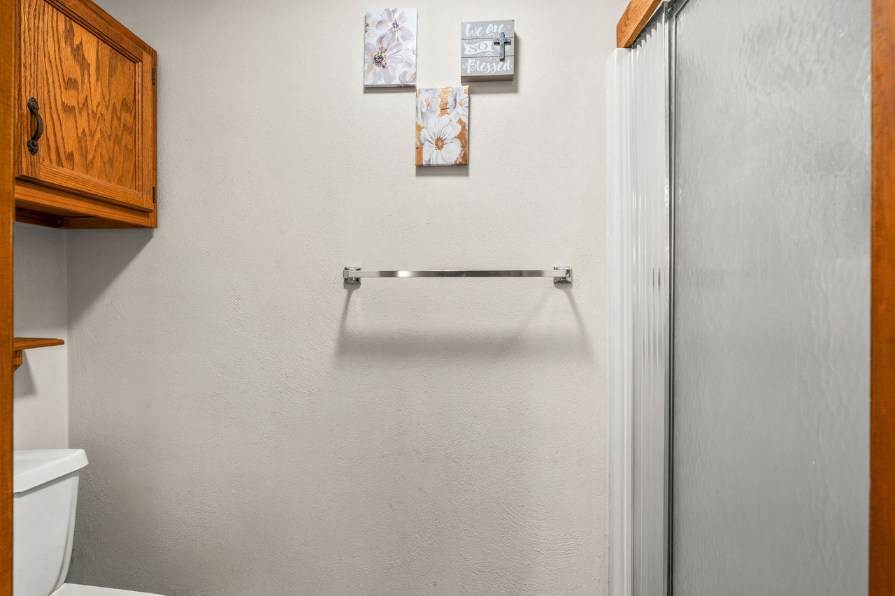 Bathroom with a frosted glass shower, wooden cabinet, and floral wall art.
