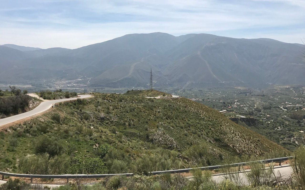 Winding road across a scrub-covered hillside overlooking a broad valley and mountain range.