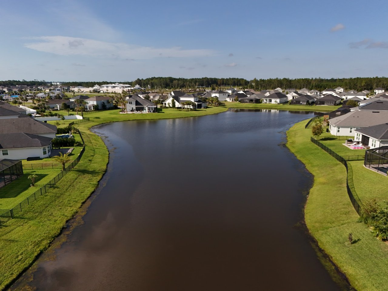 Aerial view of homes along a lake with green lawns and fenced yards.