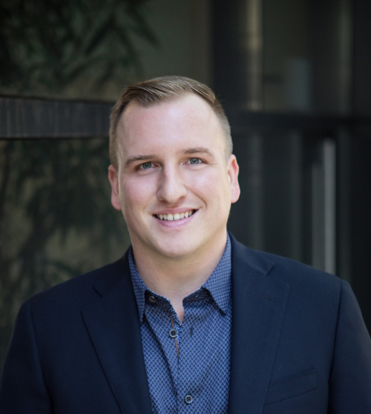 Chris Pavlin smiling in a navy blazer and patterned blue shirt.