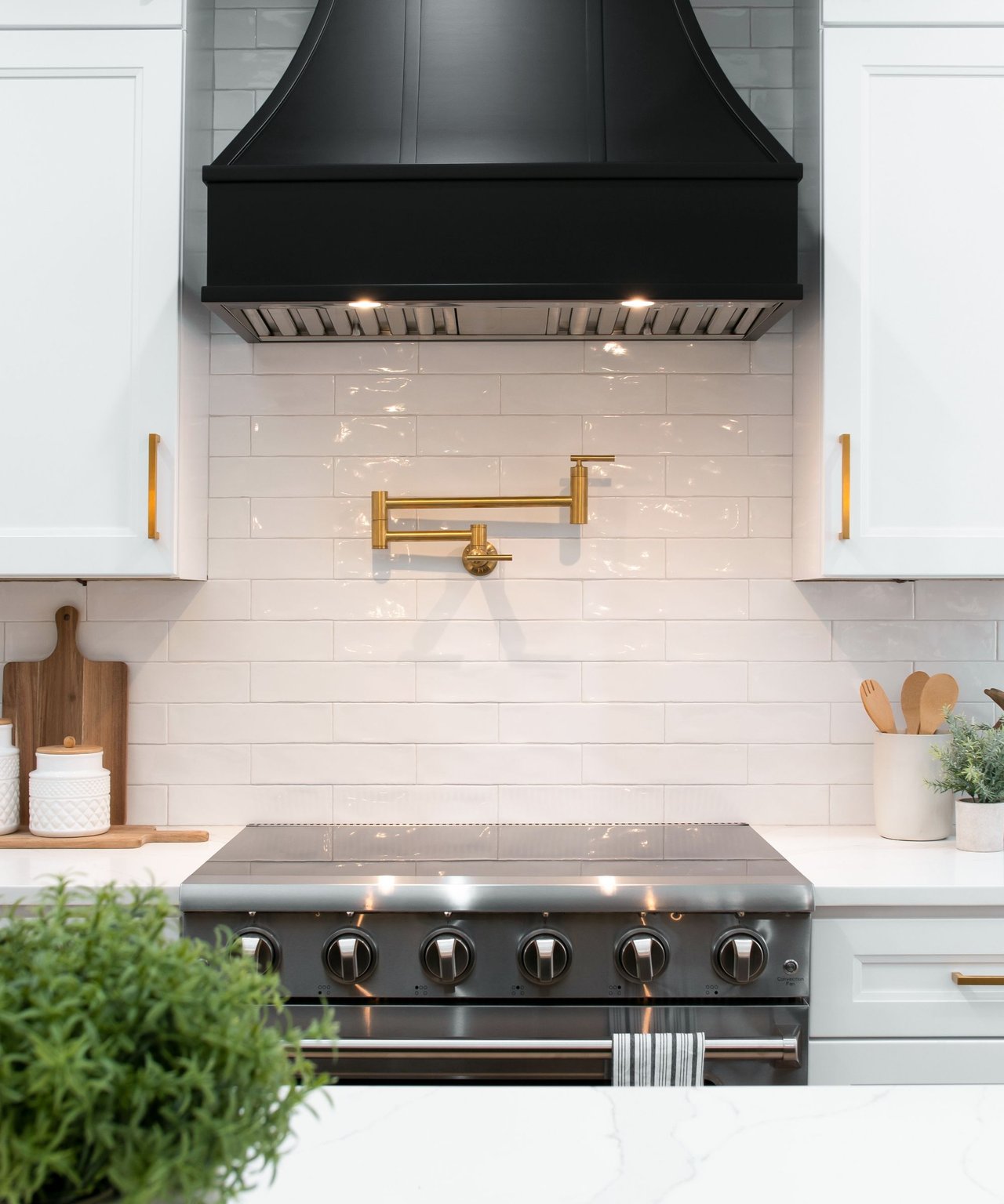 Kitchen range beneath a black hood, with white subway tile and a brass pot filler.