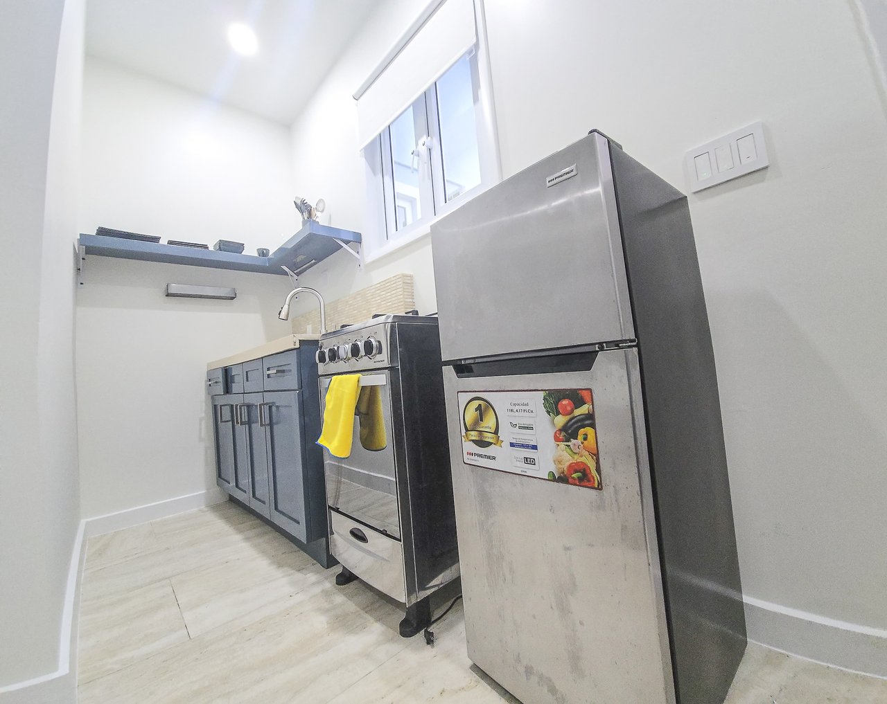 Compact kitchen with dark blue cabinets, stainless-steel stove and refrigerator, and a small high window.