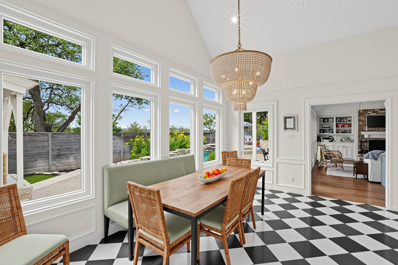 Dining room with a checkerboard floor, woven chairs, and tall windows overlooking the yard.