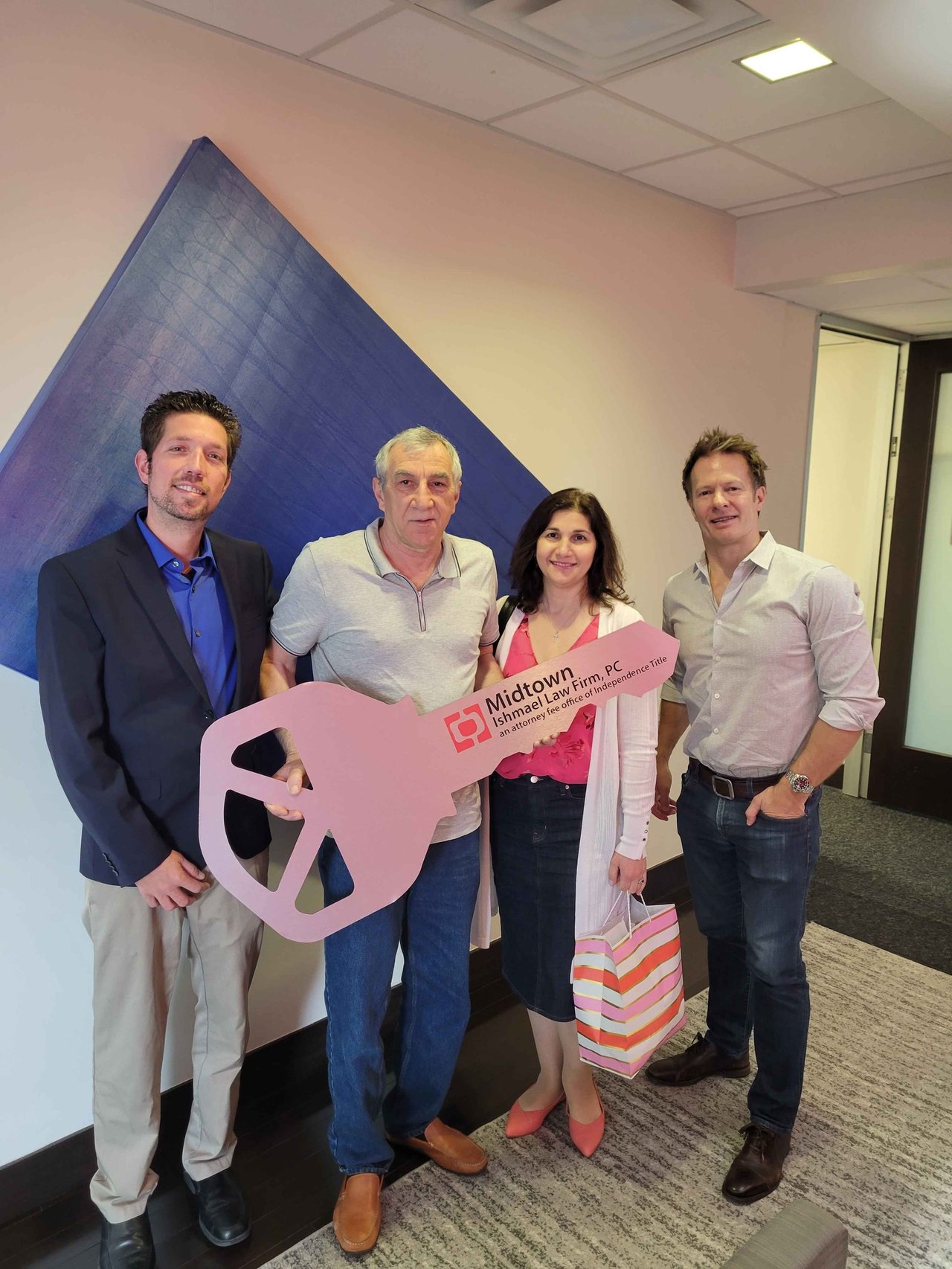 Four adults pose with a large pink Midtown Ishmael Law Firm key sign.