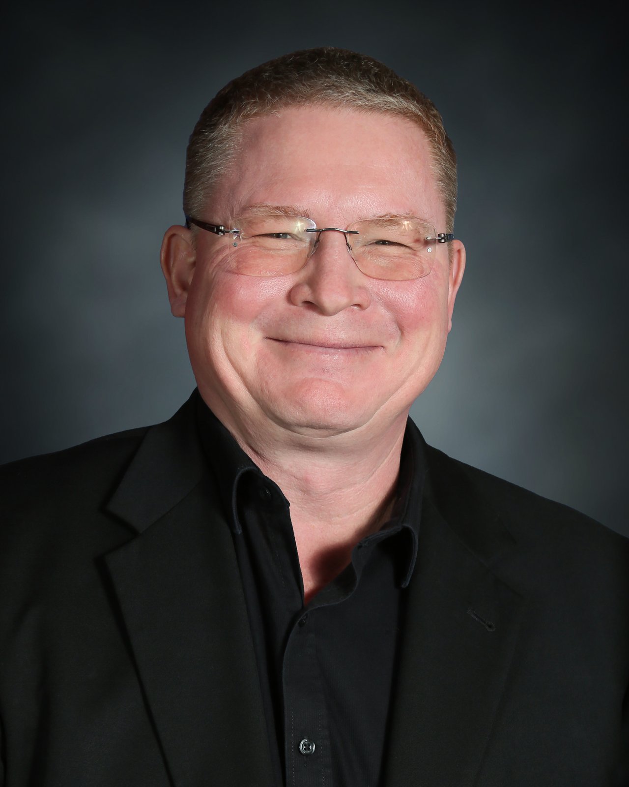 Tim Fitzgerald smiling in glasses and a black jacket.