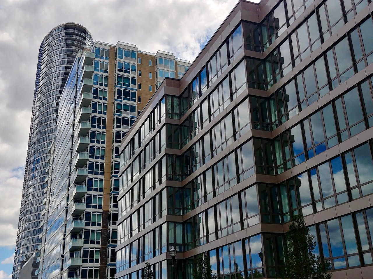 Modern condominium towers with glass façades and balconies beneath a cloudy sky.