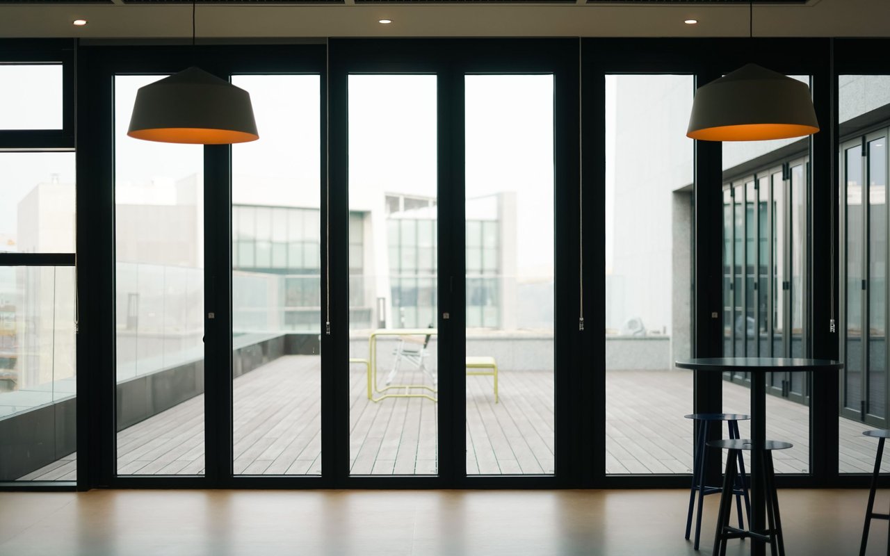 Modern interior with black-framed glass doors opening onto a rooftop terrace and neighboring buildings.