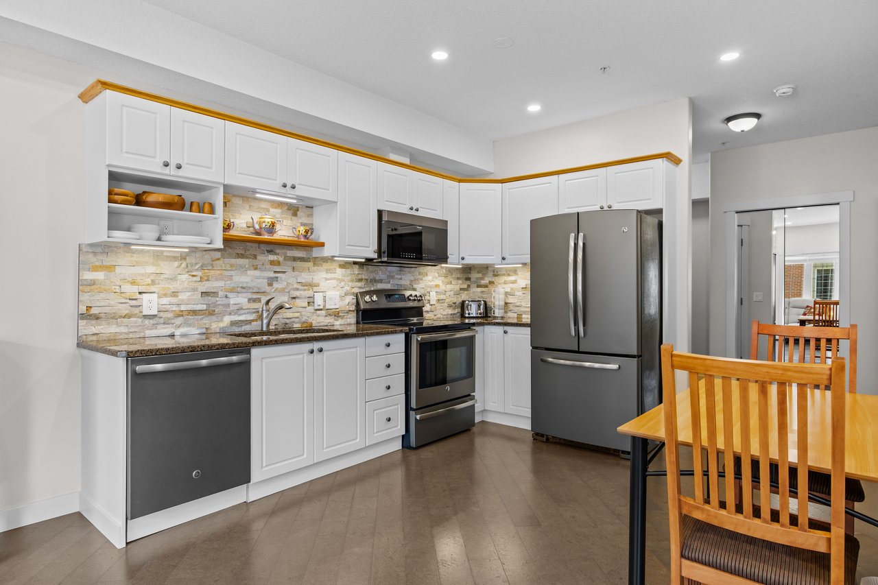 Kitchen with white cabinets, stone backsplash, dark stainless steel appliances, and a wooden dining set.