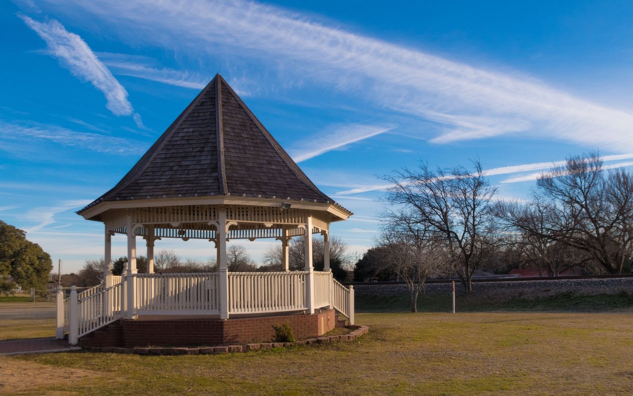 White octagonal gazebo with a steep dark roof in an open grassy area.