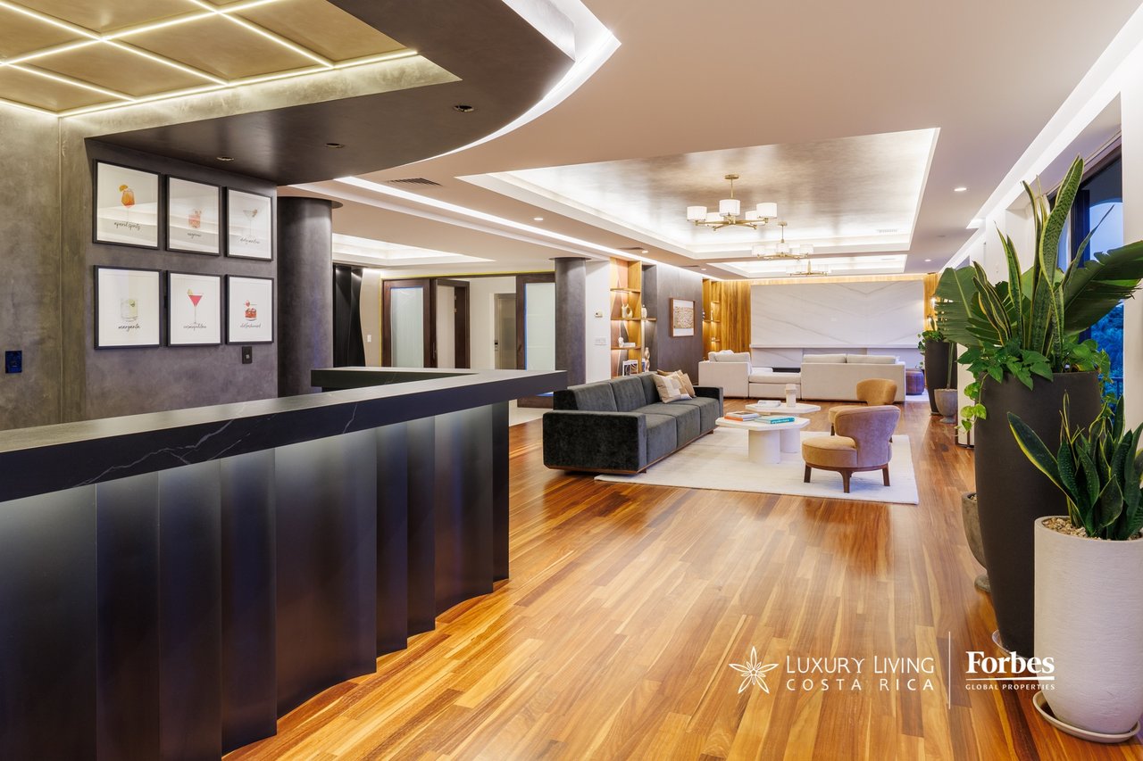 Furnished penthouse lounge with a dark reception counter, wood floors, and dramatic recessed ceiling lighting.