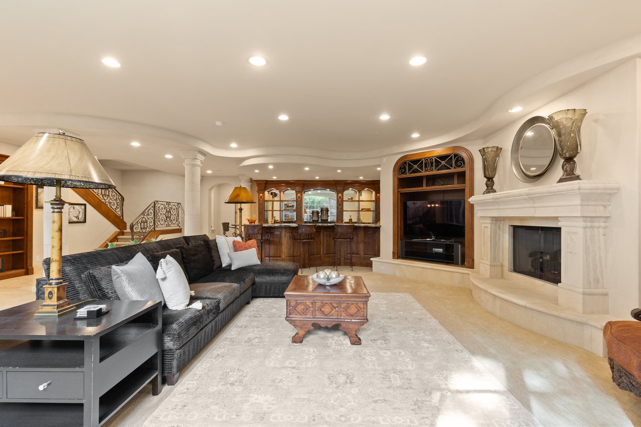 Living room with a dark sectional, built-in wooden bar, and white marble fireplace.
