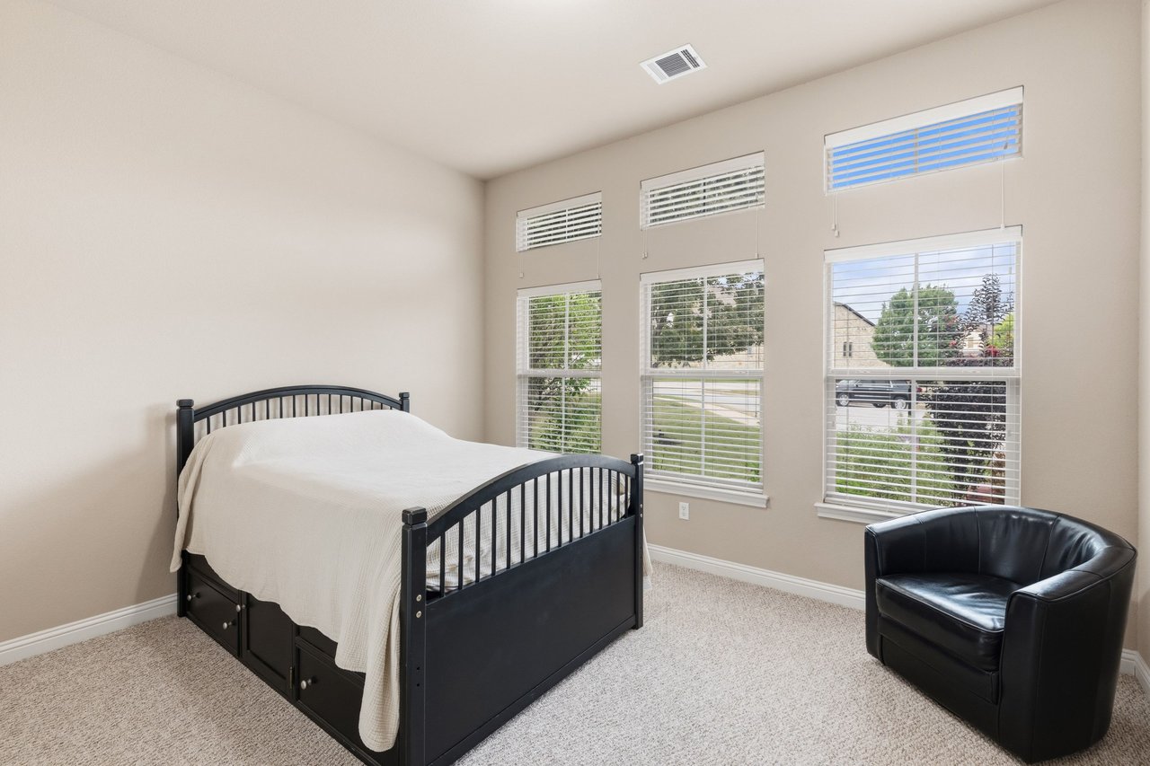 Bedroom with a black bed, white bedding, and three tall windows with blinds.