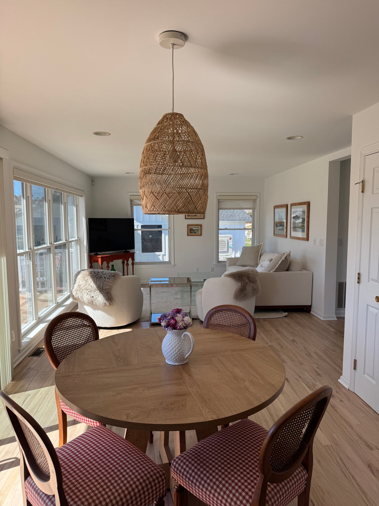 Open-plan living and dining room with a woven pendant, round table, and sunlit windows.