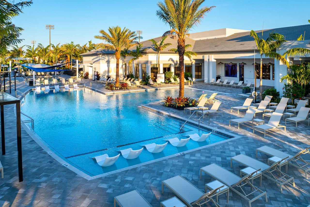 Community pool with in-water loungers, palm trees, and a clubhouse.