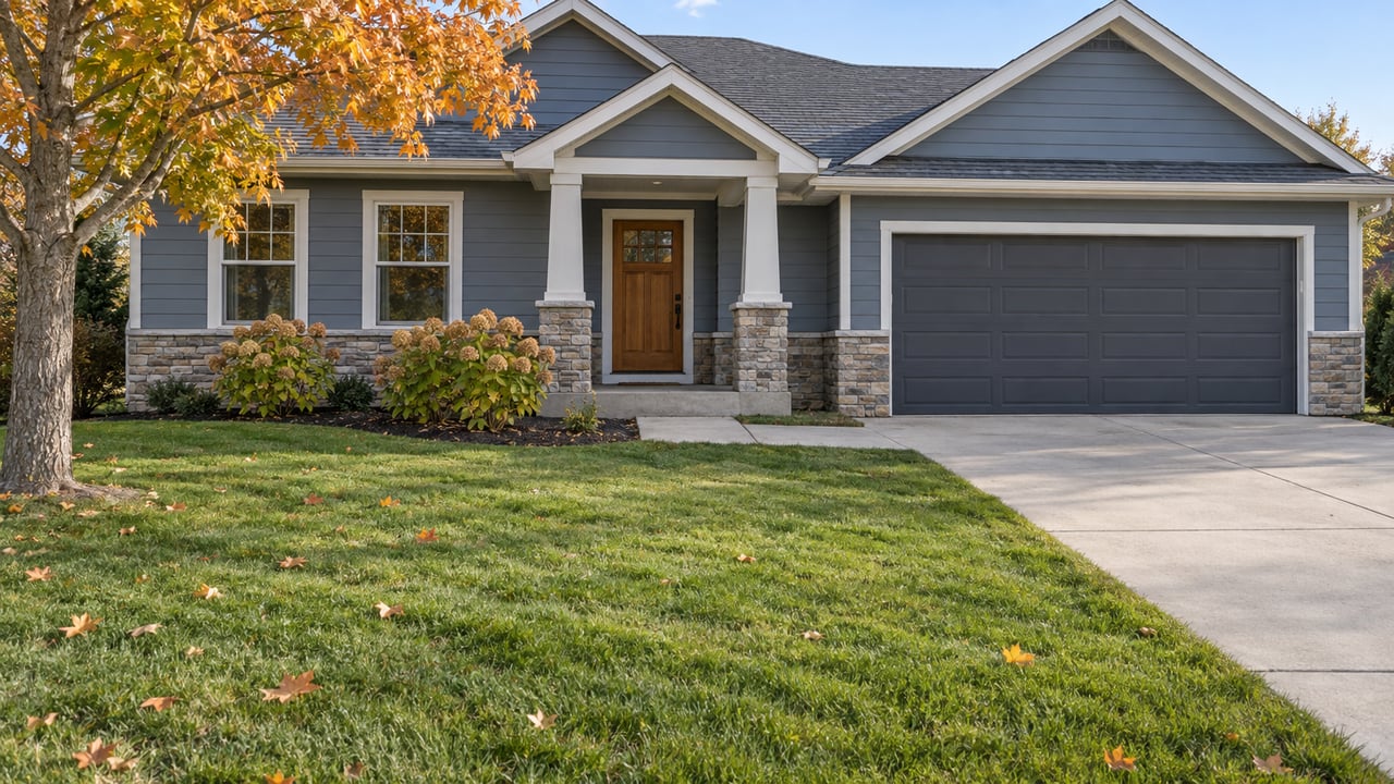 Blue-gray gabled home with a stone-based porch, attached garage and deep front lawn beneath an autumn sugar maple.
