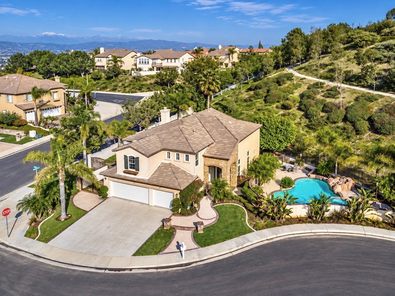 Aerial view of a beige home with a tile roof, landscaped yard, and backyard pool.