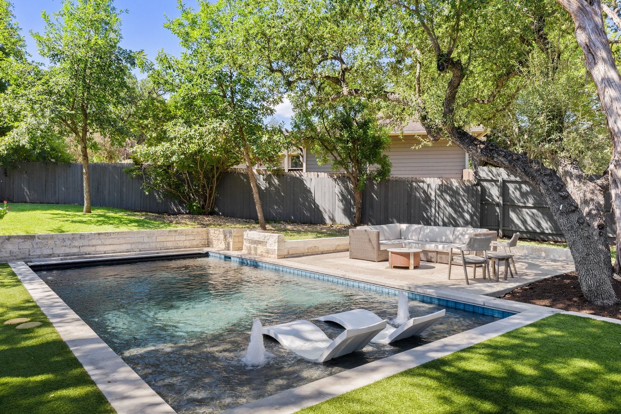 Backyard pool with in-water loungers, stone deck, and shaded patio seating.