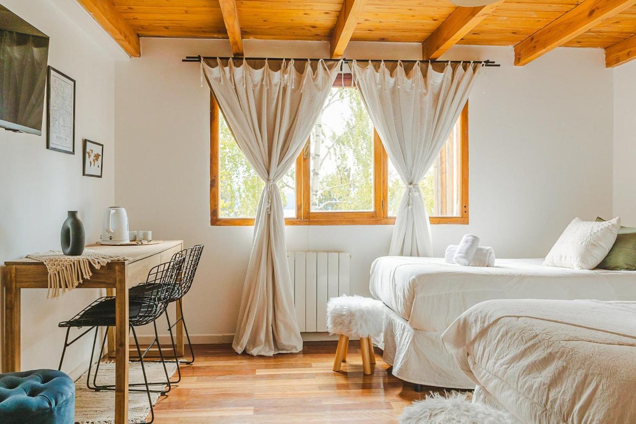 Boutique hotel bedroom with white beds, a timber-beamed ceiling, and sheer curtains around a large window.