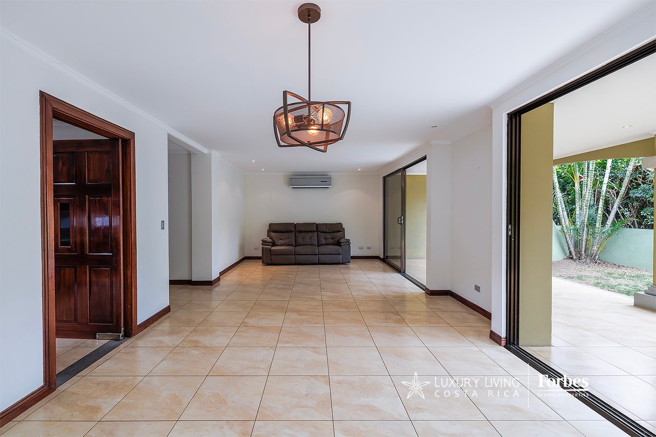 Living room with tiled floors, a dark leather sofa, and sliding doors to a garden terrace.