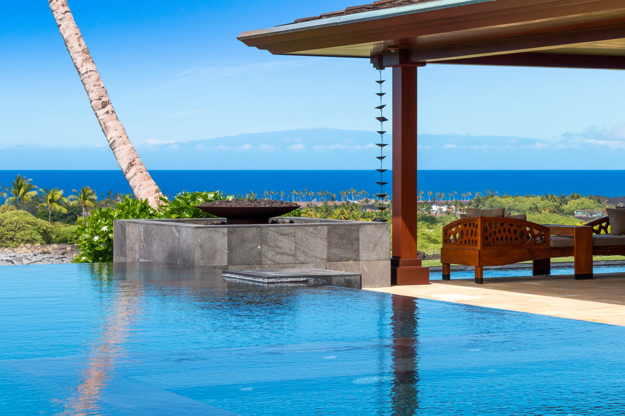 Infinity pool overlooking the ocean beside a covered patio with wooden seating.